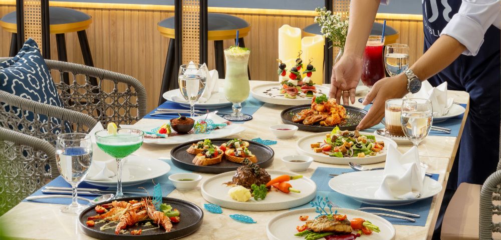Chef arranging a gourmet meal on a beautifully set dining table in a stylish restaurant.