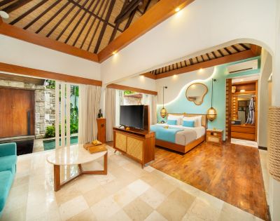 Luxurious open-plan bedroom suite featuring a wooden slatted roof and wood-paneled accents. The room includes a four-poster bed with a turquoise throw and pillows, a wall-mounted mirror, hanging lamps, a TV, wooden furniture, and a turquoise sofa. Large glass doors reveal an outdoor pool area and private entrance. The suite is finished with tile and wood flooring.
