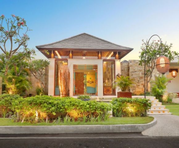 Modern villa entrance with lush greenery, elaborate door, and decorative lanterns against a clear blue sky.