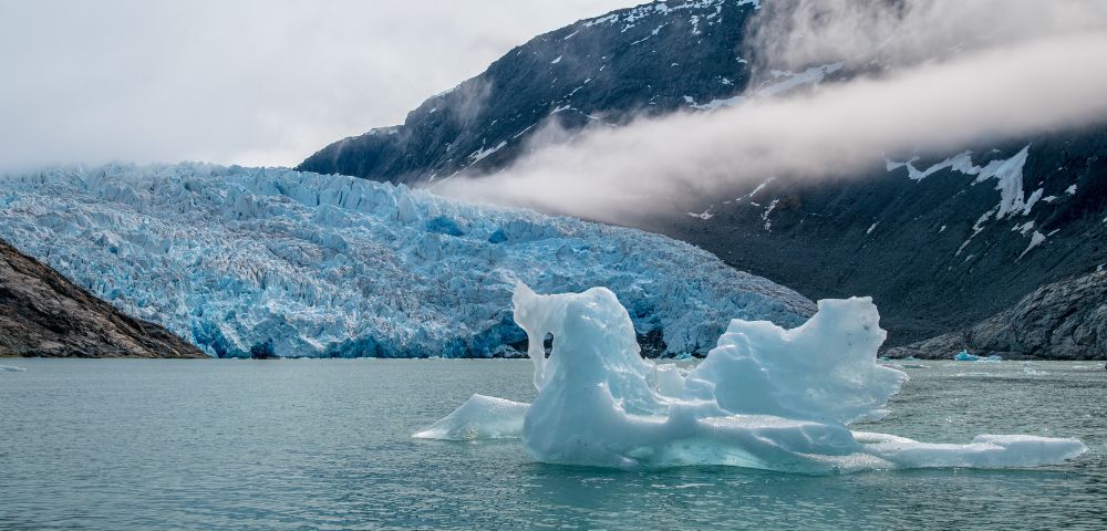 Icebergs float in calm water, surrounded by majestic mountains under a clear blue sky.