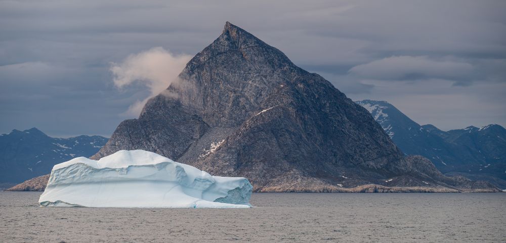 Iceberg floating, surrounded by rugged mountains and clear blue waters.