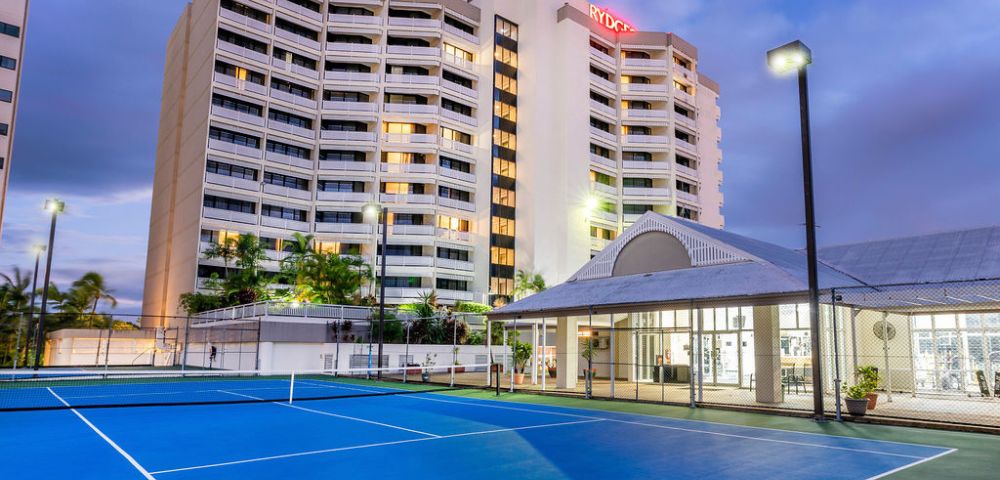 A tennis court situated in front of a large, lit up hotel building, showcasing a vibrant recreational area.