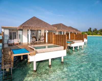 Luxurious overwater villas with thatched roofs and private pools sit above clear turquoise waters, conveying a serene and tropical vacation vibe.