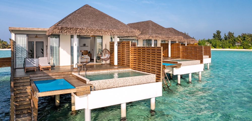 Luxurious overwater villas with thatched roofs and private pools sit above clear turquoise waters, conveying a serene and tropical vacation vibe.