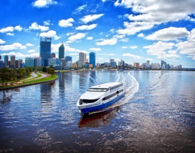 A white ferry glides along a shimmering river, with Perth's skyline and blue sky dotted with clouds in the background.