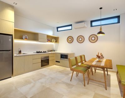Modern kitchen and dining area with beige cabinets, stainless steel appliances, and decorative plates. Wooden table with green chairs and bench, creating a cozy atmosphere.