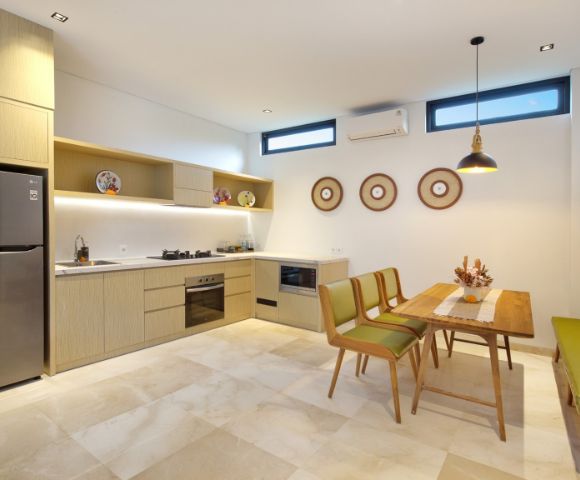 Modern kitchen and dining area with beige cabinets, stainless steel appliances, and decorative plates. Wooden table with green chairs and bench, creating a cozy atmosphere.