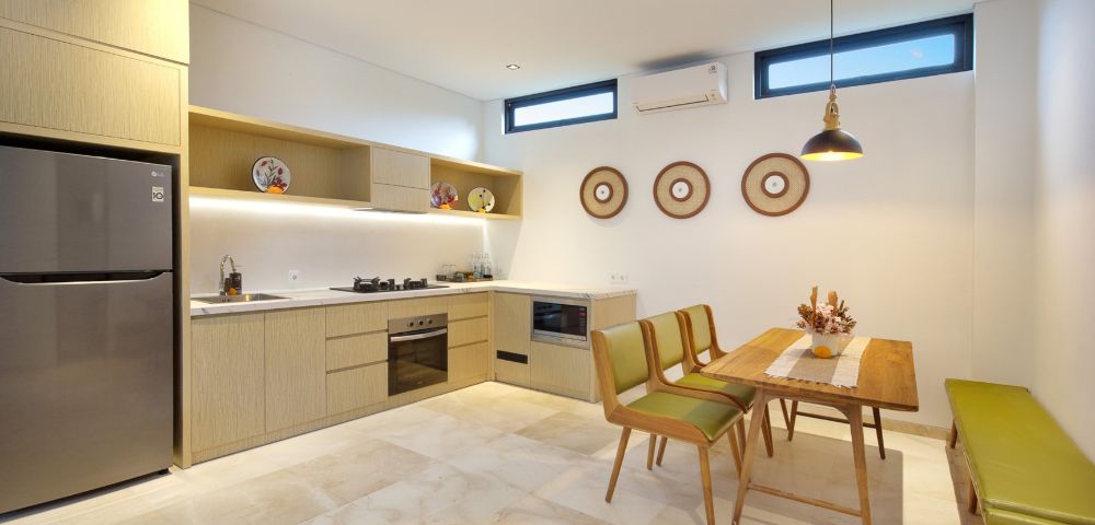 Modern kitchen and dining area with beige cabinets, stainless steel appliances, and decorative plates. Wooden table with green chairs and bench, creating a cozy atmosphere.