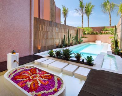 Luxurious outdoor patio featuring a sparkling pool surrounded by pink stucco walls, lush palm trees, and vibrant flowers, creating a serene oasis.