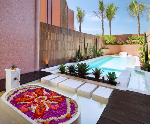 Luxurious outdoor patio featuring a sparkling pool surrounded by pink stucco walls, lush palm trees, and vibrant flowers, creating a serene oasis.