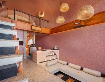 Modern interior with warm tones, featuring a split-level design. L-shaped sofa, decorative pottery, pendant lights, and textured walls create a cozy ambiance.
