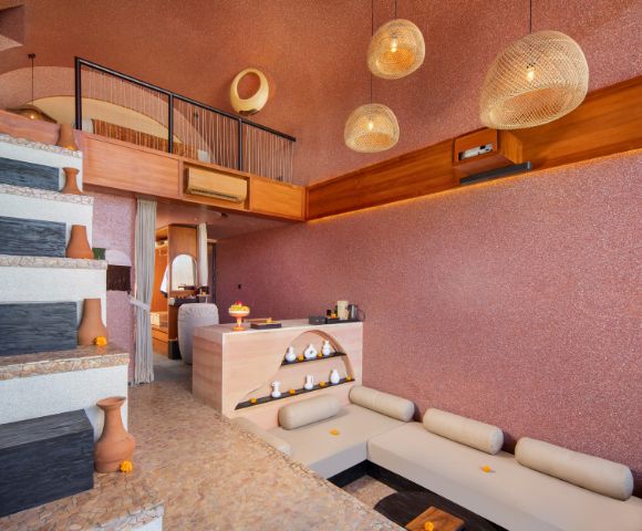 Modern interior with warm tones, featuring a split-level design. L-shaped sofa, decorative pottery, pendant lights, and textured walls create a cozy ambiance.