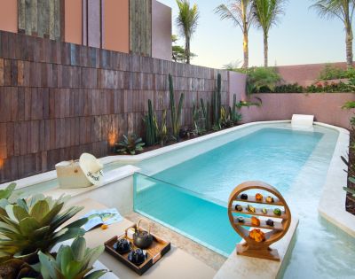 A serene pool area with tropical plants and palm trees, featuring a small waterfall, wooden decor, and a stylish tea set, evoking a peaceful, luxurious vibe.