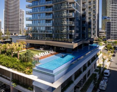 Luxurious high-rise with an elevated turquoise pool, surrounded by palm trees and loungers. Modern skyline in the background, creating a serene urban oasis.