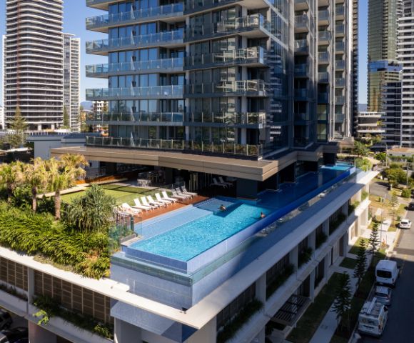 Luxurious high-rise with an elevated turquoise pool, surrounded by palm trees and loungers. Modern skyline in the background, creating a serene urban oasis.