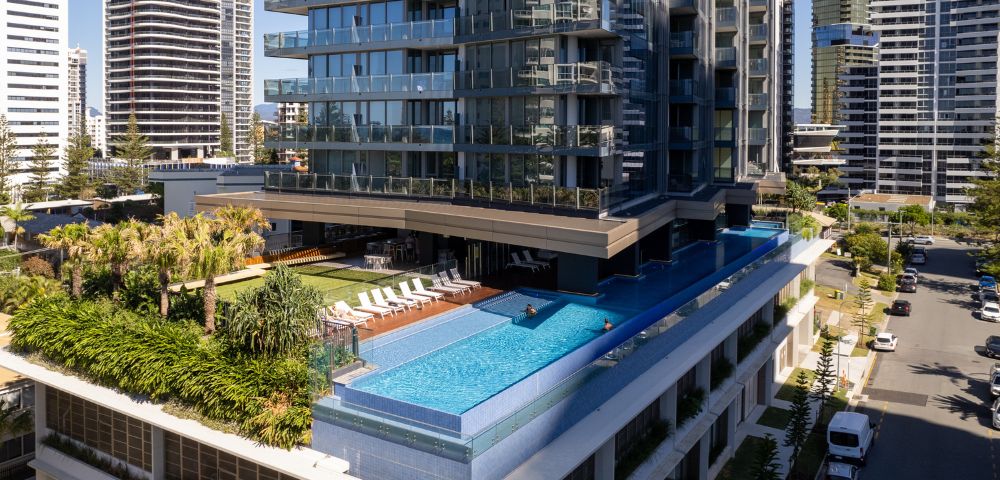 Luxurious high-rise with an elevated turquoise pool, surrounded by palm trees and loungers. Modern skyline in the background, creating a serene urban oasis.