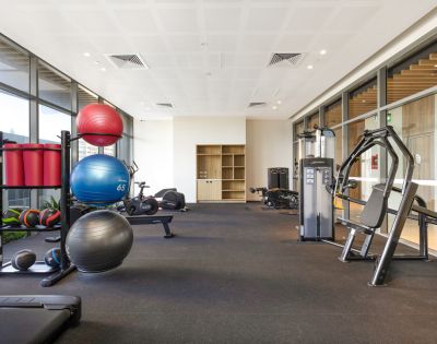 Modern gym with exercise equipment, including stability balls, weighted balls, and machines. Bright, spacious interior with large windows. Calm and inviting.