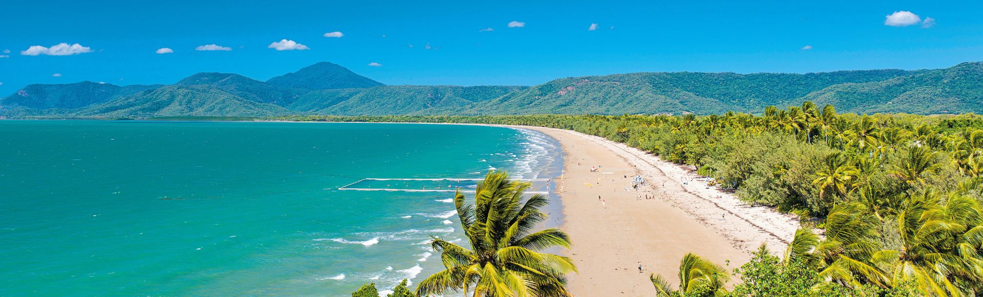 Beach view from a hilltop, showcasing sandy shores and gentle waves under a clear blue sky.