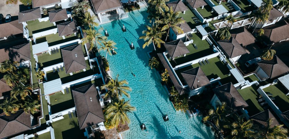 Aerial view of a resort featuring a large swimming pool surrounded by lush greenery and sun loungers.
