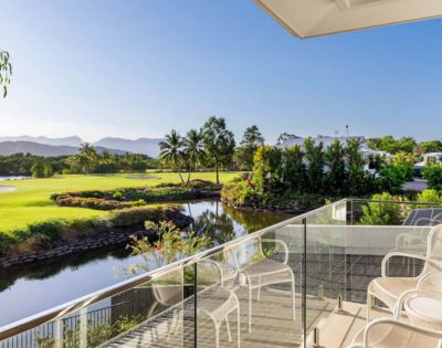 Balcony overlooking a serene golf course with lush greenery, a calm pond, and distant mountains under a clear blue sky, evoking tranquility.
