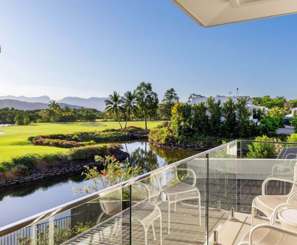 Balcony overlooking a serene golf course with lush greenery, a calm pond, and distant mountains under a clear blue sky, evoking tranquility.