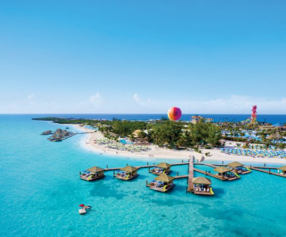 Aerial view of a tropical beach with turquoise water and floating cabanas. A hot air balloon is in the background, adding a sense of adventure.
