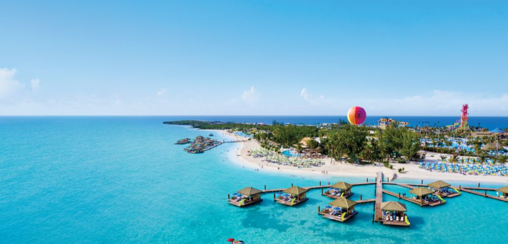 Aerial view of a tropical beach with turquoise water and floating cabanas. A hot air balloon is in the background, adding a sense of adventure.