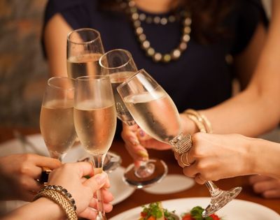 A group of people clinks champagne glasses in a celebratory toast over a dining table. The scene conveys joy and festivity, with blurred background.