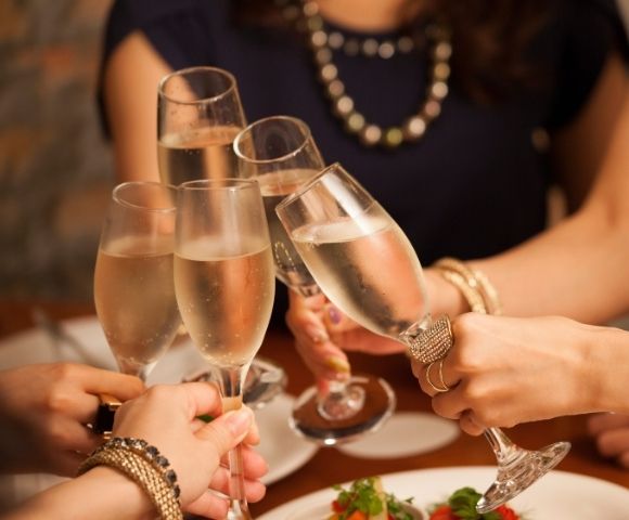 A group of people clinks champagne glasses in a celebratory toast over a dining table. The scene conveys joy and festivity, with blurred background.