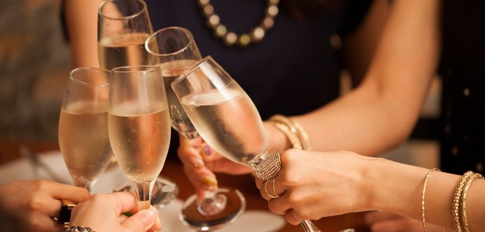 A group of people clinks champagne glasses in a celebratory toast over a dining table. The scene conveys joy and festivity, with blurred background.