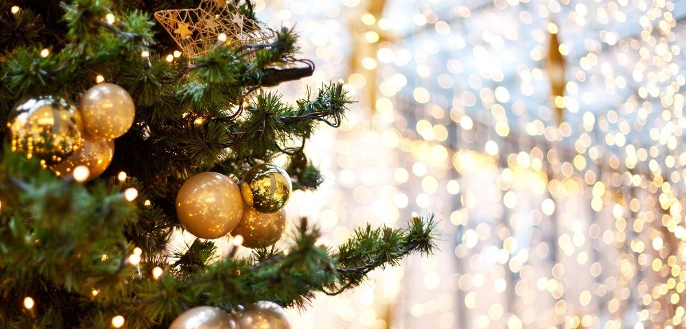 Christmas tree adorned with gold baubles, a star ornament, and twinkling lights. The background glows softly, creating a warm, festive ambiance.