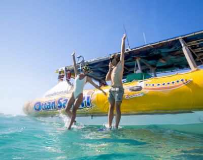 Two people in swimsuits joyfully leap from a yellow boat labeled 