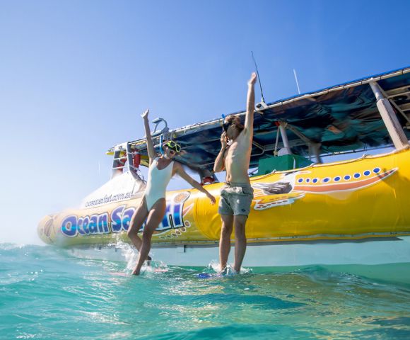 Two people in swimsuits joyfully leap from a yellow boat labeled 