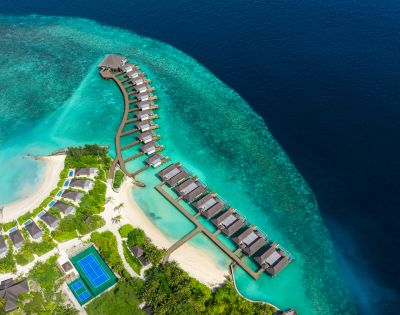 Aerial view of a luxurious resort featuring overwater bungalows, turquoise waters, and lush greenery on the shore.