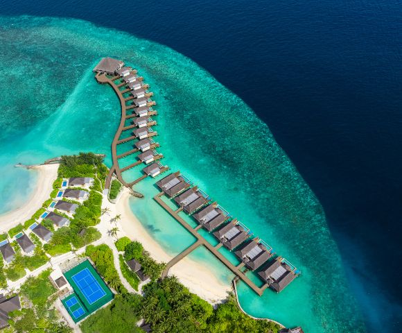 Aerial view of a luxurious resort featuring overwater bungalows, turquoise waters, and lush greenery on the shore.