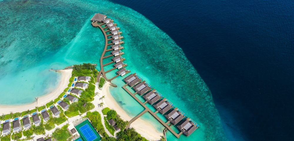 Aerial view of a luxurious resort featuring overwater bungalows, turquoise waters, and lush greenery on the shore.