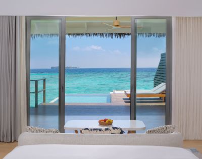 View from a modern bedroom showcasing a sliding glass door to a private deck with a pool and turquoise ocean beyond.