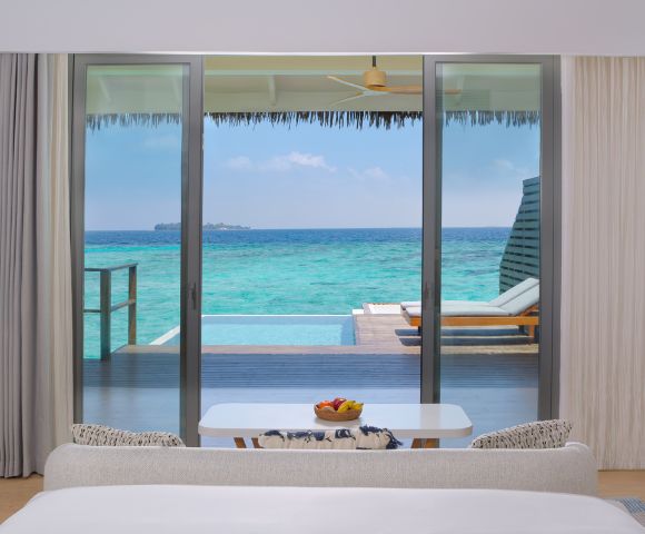 View from a modern bedroom showcasing a sliding glass door to a private deck with a pool and turquoise ocean beyond.