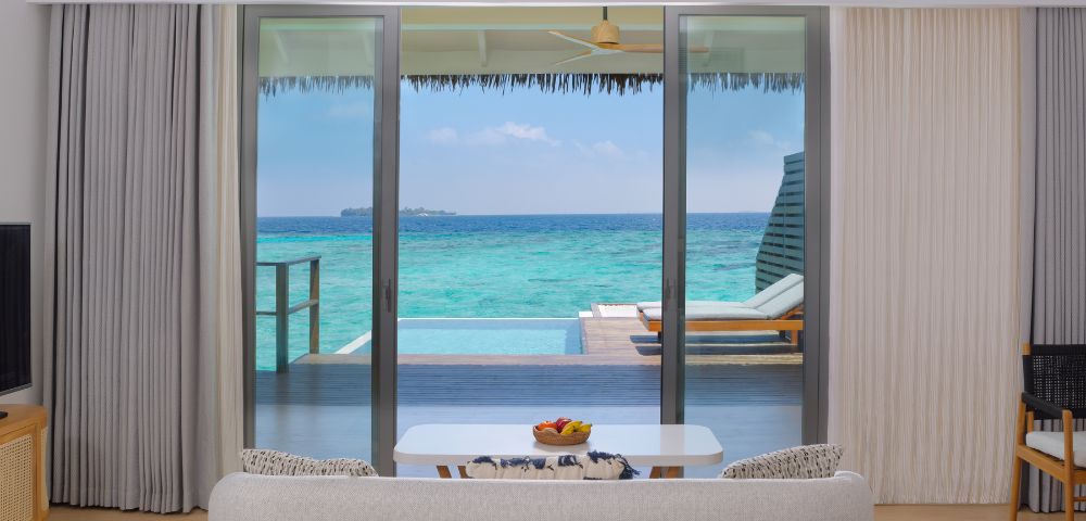View from a modern bedroom showcasing a sliding glass door to a private deck with a pool and turquoise ocean beyond.