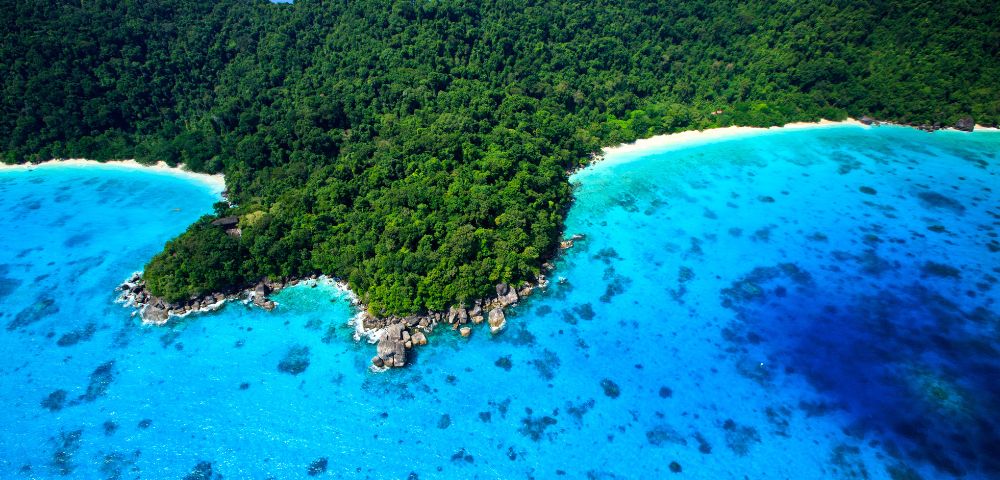 Aerial view of a lush green island surrounded by crystal-clear turquoise waters and white sandy beaches in Mu Ko Similan National Park, Phang Nga.