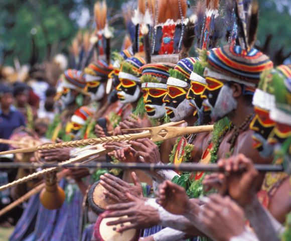 A vibrant line of dancers with painted faces and colorful headdresses playing traditional instruments at a cultural festival.