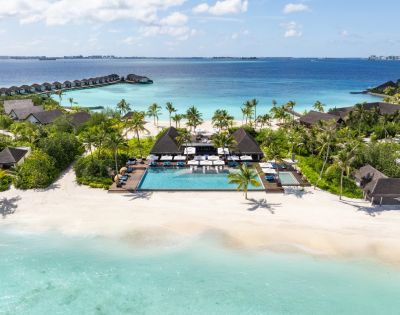 Aerial view of a tropical resort with a pool, sun loungers, and palm trees, adjacent to a pristine beach and turquoise ocean.