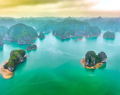 Aerial view of Ha Long Bay, Vietnam, showcasing emerald waters dotted with lush, limestone islands under a hazy sky, evoking tranquility and grandeur.