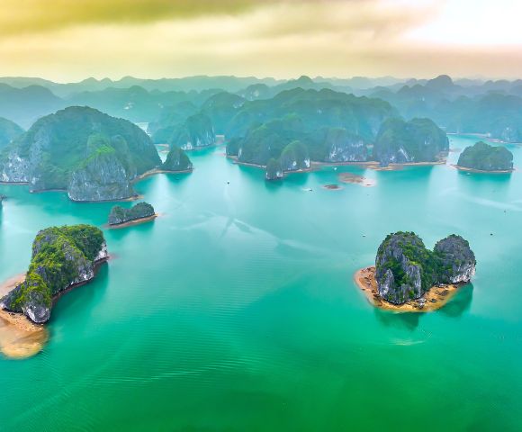 Aerial view of Ha Long Bay, Vietnam, showcasing emerald waters dotted with lush, limestone islands under a hazy sky, evoking tranquility and grandeur.