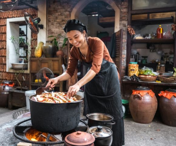 A woman cooking food in a traditional way using charcoal in the kitchen.