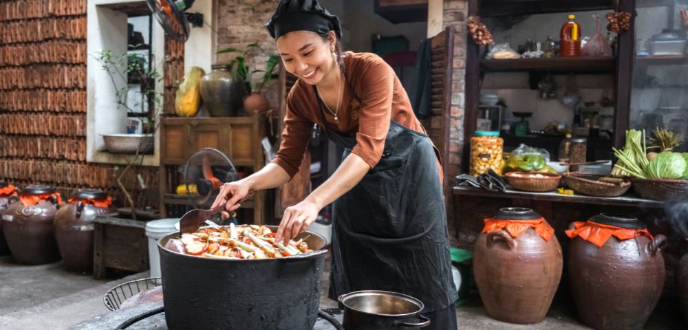 A woman cooking food in a traditional way using charcoal in the kitchen.