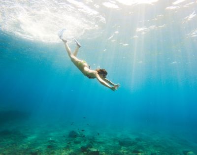 A person in a swimsuit dives gracefully underwater in clear blue ocean, with sunlight streaming down, creating a serene and adventurous atmosphere.