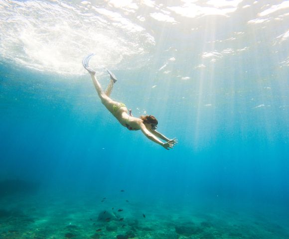 A person in a swimsuit dives gracefully underwater in clear blue ocean, with sunlight streaming down, creating a serene and adventurous atmosphere.