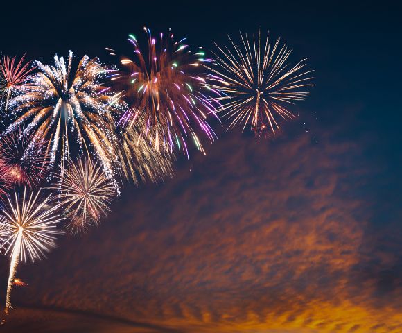 A vibrant fireworks display illuminates the night sky with colorful bursts, set against a serene backdrop of twilight clouds, evoking a festive atmosphere.