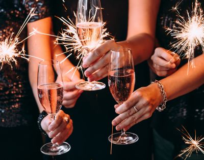 Hands holding sparklers and champagne glasses, creating a festive, celebratory atmosphere. The scene is lively with sparkling lights and bubbly drinks.